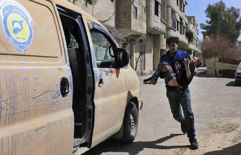 A member of  the Syrian Civil Defense group  in Ghouta, Syria, carries a boy who was wounded during airstrikes and shelling by Syrian government forces Sunday.