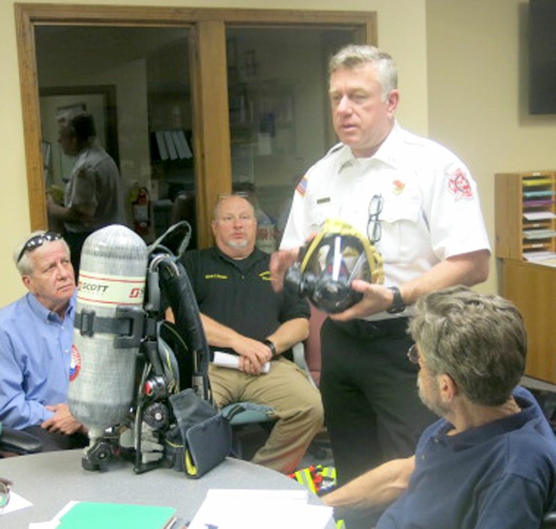 Westside Eagle Observer/SUSAN HOLLAND Lonnie Mullen, Gravette Fire Department chief (standing), displays one of the 19 new Airpaks recently purchased for use by the department. Mullen said the units were badly needed to ensure the firemen's safety as older units had failed on recent fire calls. Listening to Mullen's presentation are Carl Rabey, city finance director; Chuck Skaggs, chief of police; and Mike von Ree, city clerk.