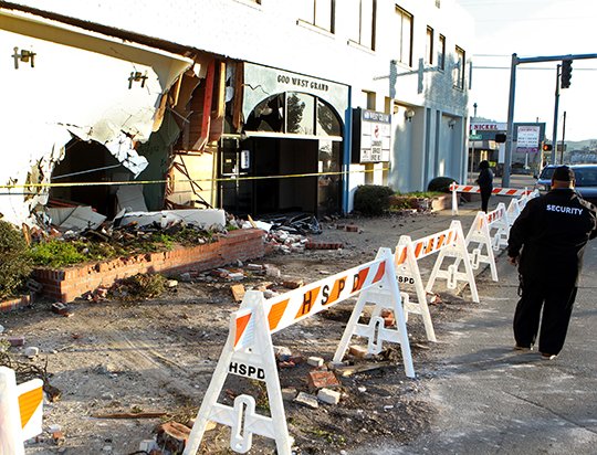 The Sentinel-Record/Richard Rasmussen WRECK AFTERMATH: A security guard walks past 600 W. Grand Ave. Tuesday morning after an allegedly stolen Dodge Challenger crashed into the side of the building while fleeing from Hot Springs police. The driver, identified as Noah Christopher Merritt, 18, and his 14-year-old nephew were both injured.