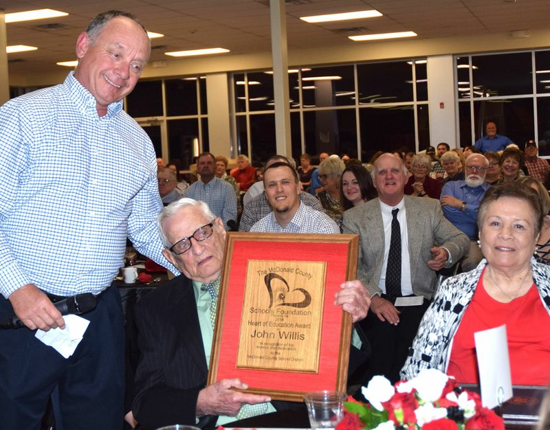 PHOTO BY RICK PECK/SPECIAL TO MCDONALD COUNTY PRESS John Willis (center) is presented with the 2018 Heart of Education Award by Randall Smith, secretary of the McDonald County Schools Foundation. Willis served as principal at McDonald County High School for 24 years. Willis was accompanied to the banquet by his wife, Lola (right), his four children and numerous grandchildren.