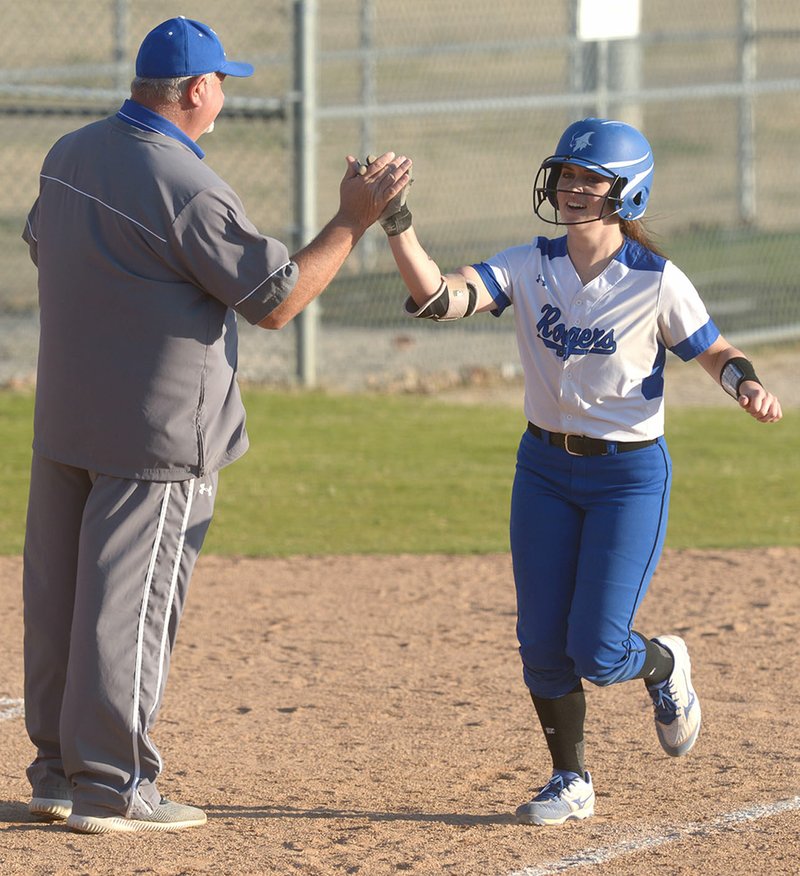 NWA Democrat-Gazette/ANDY SHUPE Rogers High's Courtney Storey (right) is congratulated by coach Mike Harper on Thursday as she rounds third base after hitting a home run against Rogers Heritage at Veterans Park in Rogers. Visit nwadg.com/photos for more photos from the game.