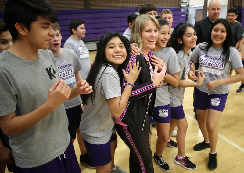 NWA Democrat-Gazette/DAVID GOTTSCHALK Amy Lee, physical education teacher at Oakdale Middle School, is hugged by her students Thursday after learning she received a $23,875 grant from the Rogers Public Education Foundation for outdoor education in the gym at the school in Rogers. This is the third grant paid for by a special bequeathment of local outdoors enthusiast George Merwin, who left more than $100,000 to the foundation when he died in 2014. The grant will buy equipment including climbing wall mats, bikes, longboards and camping equipment.