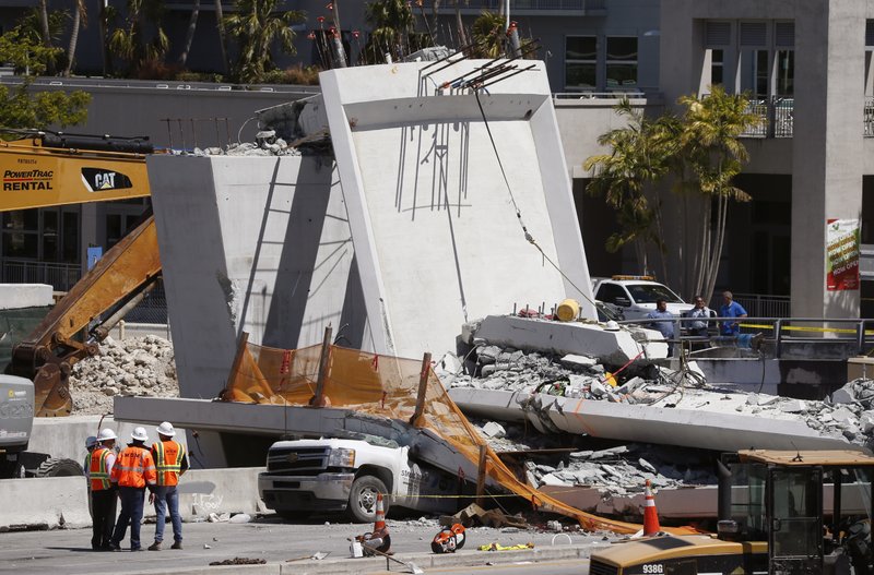 Workers stand next to a section of a collapsed pedestrian bridge, Friday, March 16, 2018 near Florida International University in the Miami area. The new pedestrian bridge that was under construction collapsed onto a busy Miami highway Thursday afternoon, crushing vehicles beneath massive slabs of concrete and steel, killing and injuring several people, authorities said. 