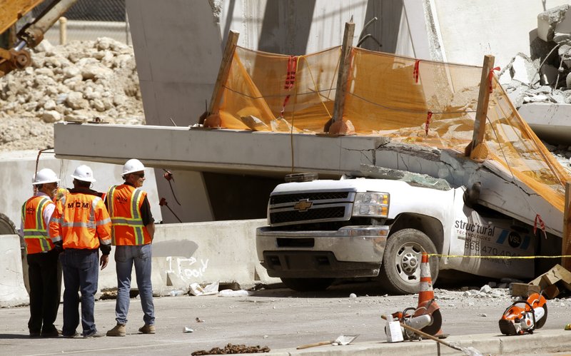 Workers stand next to a section of a collapsed pedestrian bridge, Friday, March 16, 2018 near Florida International University in the Miami area. The new pedestrian bridge that was under construction collapsed onto a busy Miami highway Thursday afternoon, crushing vehicles beneath massive slabs of concrete and steel, killing and injuring several people, authorities said. (AP Photo/Wilfredo Lee)