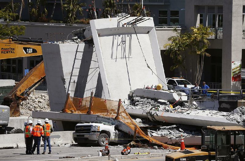 Workers in Miami stand next to a section of a collapsed pedestrian bridge near Florida International University on Friday. Two days before Thursday’s collapse, an engineer had left a voice mail at the state transportation agency noting cracks in the concrete.
