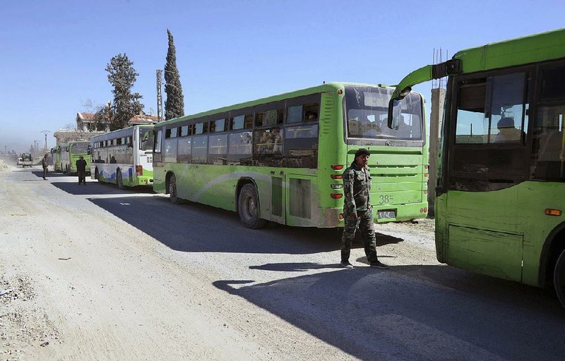 Syrian troops stand guard Friday near buses carrying Syrian civilians fl eeing the fi ghting between Syrian government forces and rebels near Hamouria.
