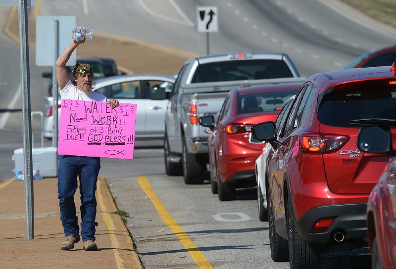 Daniel Nelson sells bottles of water Thursday at Joyce Boulevard and College Avenue in Fayetteville. The City Council is considering whether to designate medians as part of a “roadway” under an ordinance that bans people from standing or walking in the street.