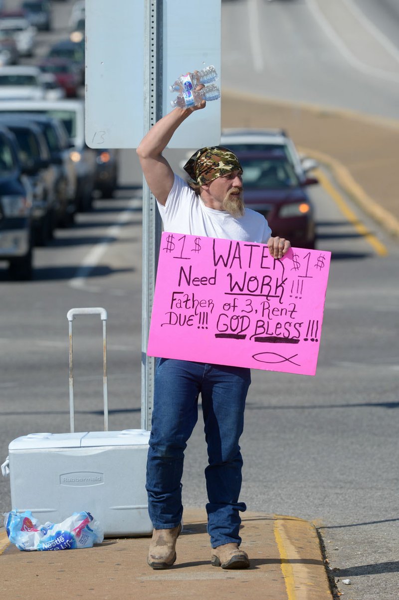 NWA Democrat-Gazette/ANDY SHUPE Daniel Nelson, a former construction worker originally from Washington, sells bottles of water Thursday at the intersection of Joyce Boulevard and College Avenue in Fayetteville. Nelson, who has struggled with addiction and with drug users at job sites, supports his family by selling water to motorists at the intersection. Fayetteville's City Council is considering adopting an amendment to city code defining the term "roadway" as from far curb to far curb. The change aims to promote safety by preventing people from standing in the middle of a road.