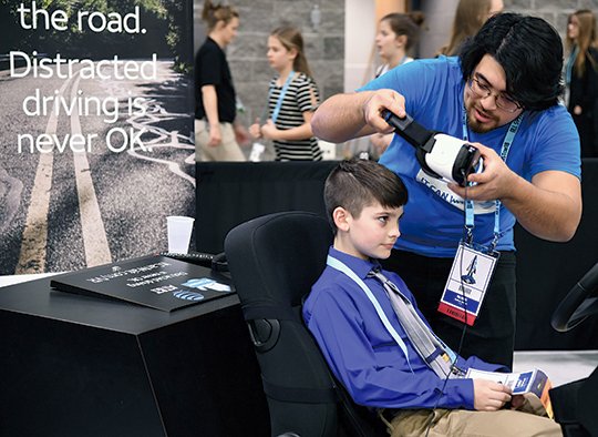 The Sentinel-Record/Grace Brown TEXTING AND DRIVING: AT&T Brand Ambassador Joshua James, right, sets Harley Steele, 9, of Newark, up for the AT&T texting and driving virtual reality simulator during the EAST Conference at the Hot Springs Convention Center on March 14. The simulator is part of AT&T's "It Can Wait" campaign.