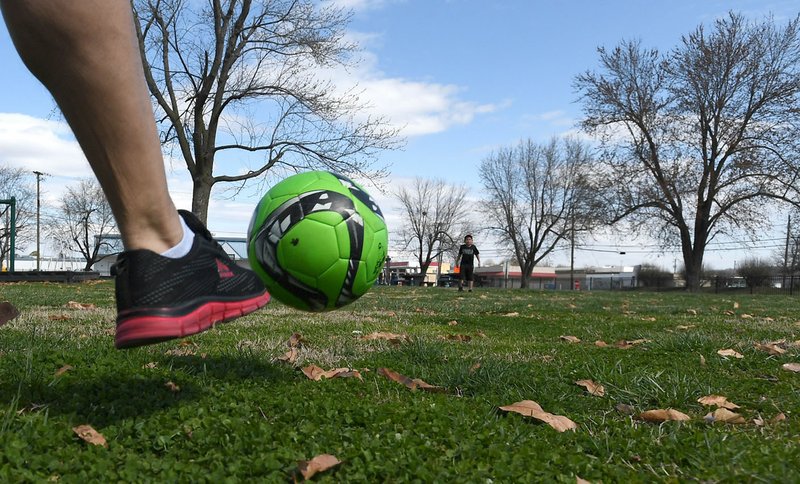 Jesus Pascual of Springdale kicks a ball to his son Pedro Pascual, 9, on Monday at Luther George Park in Springdale. The park, near downtown, features pavilions, exercise equipment, playgrounds, a skate park and open grass areas.
