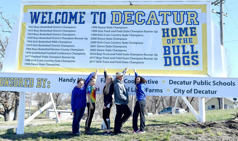 Westside Eagle Observer/SUBMITTED Members of the 2017 Decatur girls' 1A state championship track team point to their accomplishment on the new "Welcome to Decatur" sign on Highway 59 South in Decatur March 14. Team members include Paige Barrett (left), Destiny Mejia, Paige Vann, Coach Shane Holland, and Desi Meek. Not pictured were Cameron Shaffer and Meagan Smith.