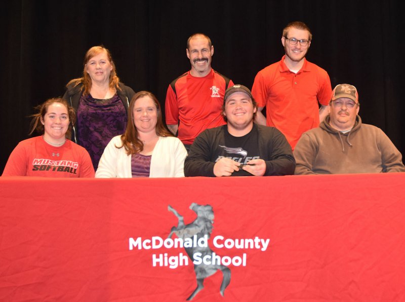 RICK PECK/SPECIAL TO MCDONALD COUNTY PRESS Tinker Kinser, (sitting, third from left) a senior at McDonald County High School, signs a letter of intent to wrestle at the University of the Ozarks in Clarksville, Ark. Front row, left to right: Whitney Kinser (sister), Valerie Kinser (mom), Tinker Kinser and Bronnie Kinser (dad). Back row: Beth Kinser (grandmother), Josh Factor (MCHS head wrestling coach) and Cody Factor (MCHS assistant wrestling coach).