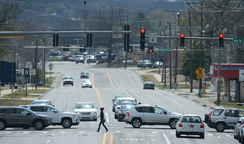 A pedestrian crosses School Avenue on Friday as traffic passes on Martin Luther King Jr. Boulevard in Fayetteville. Consulting firm Nelson/Nygaard wrapped up a nearly two-year-long study on all modes of travel in the city and presented its findings to the City Council on Tuesday.