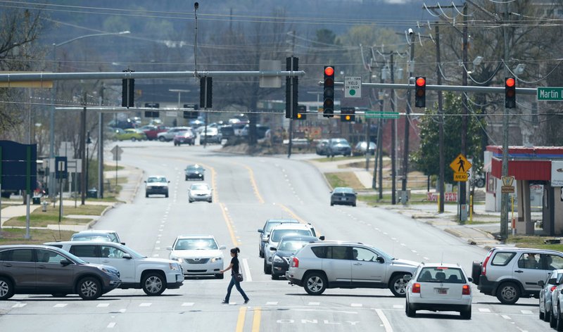 A pedestrian crosses School Avenue Friday as traffic passes on Martin Luther King Jr. Boulevard in Fayetteville. 