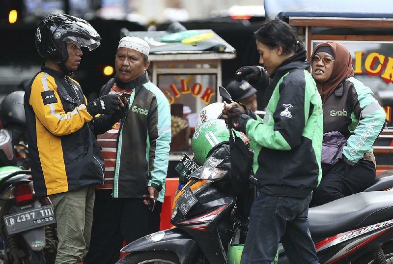 An Uber rider talks with a Grab rider in Jakarta, Indonesia, on Monday. Ride-hailing giant Uber is selling its business in Southeast Asia to regional rival Grab in its latest withdrawal from a daunting overseas market.  