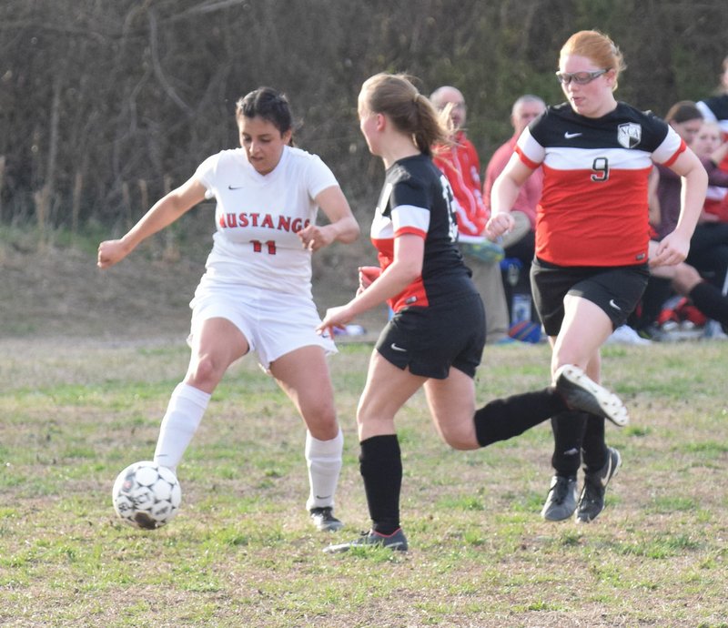 RICK PECK/SPECIAL TO MCDONALD COUNTY PRESS McDonald County's Aalliyah Rubio makes a pass while being attacked by a pair of New Covenant defenders during the Lady Mustangs' 1-0 loss on March 23 at MCHS.