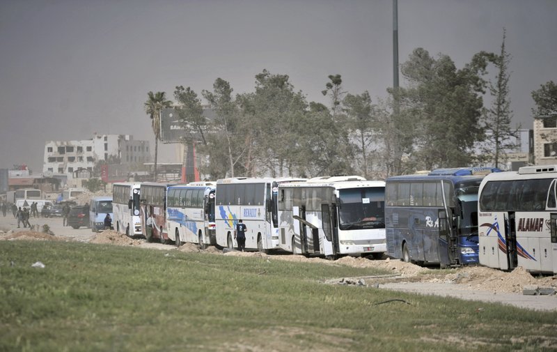 This photo released by the Syrian official news agency SANA, shows a convoy of buses carrying rebel fighters and their families leaving several towns and villages that are to be handed over to government control, in the eastern Ghouta region near Damascus, Syria, Wednesday, March. 28, 2018. U.N. coordinator Ali al-Za'atari says at least 80,000 people have fled the government's offensive in the eastern Ghouta suburbs, where shelling and airstrikes have killed hundreds of people in recent weeks. He says 50,000 are still living in shelters, with many requiring medical care. (SANA via AP)