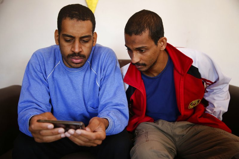 Alexanda Amon Kotey, left, and El Shafee Elsheikh, who were allegedly among four British jihadis who made up a brutal Islamic State cell dubbed "The Beatles," read a news article about themselves during an interview with The Associated Press at a security center in Kobani, Syria, Friday, March 30, 2018. The men said that their home country’s revoking of their citizenship denies them fair trial. “The Beatles” terror cell is believed to have captured, tortured and killed hostages including American, British and Japanese journalists and aid workers. (AP Photo/Hussein Malla)