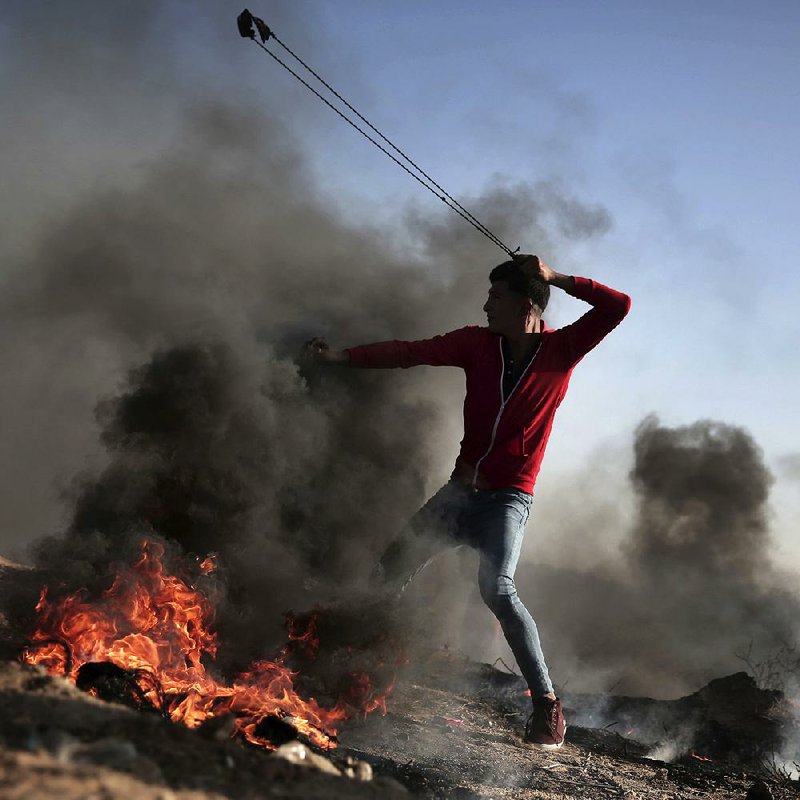 A Palestinian protester slings a stone at Israeli soldiers Saturday during a clash near the border of Israel and the Gaza Strip. The soldiers responded with live fire and tear gas.