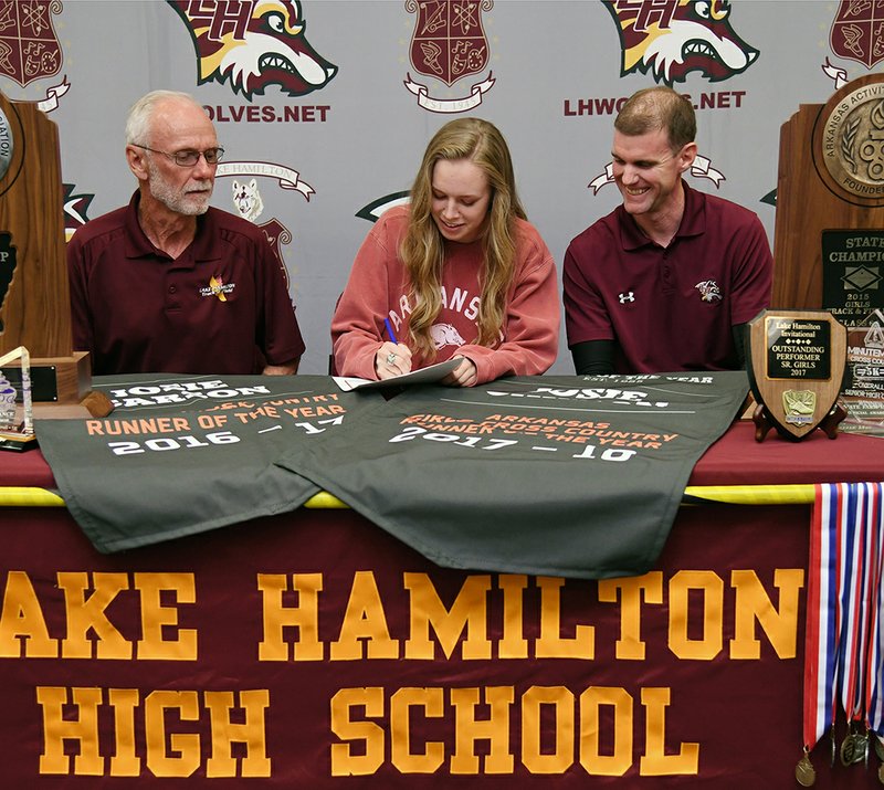 The Sentinel-Record/Grace Brown NOT SLOWING DOWN: Josie Carson, center, signs her national letter of intent to run cross country and track with the Arkansas Razorbacks as Lake Hamilton head coach Karl Koonce, left, and assistant coach Brandon Smith look on Tuesday. Carson, one of the most decorated athletes in Lake Hamilton history, won a record fourth straight cross country individual title in November and has twice been named the Gatorade Cross Country Athlete of the Year.