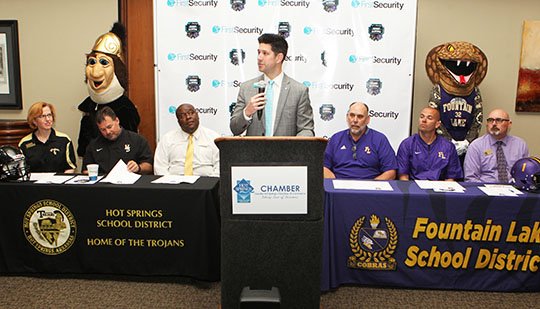 The Sentinel-Record/Richard Rasmussen CLASSIC KICKOFF: Scott Dews, center, president of First Security Bank in Hot Springs, speaks during Tuesday's announcement at The Greater Hot Springs Chamber of Commerce for the First Security Bank Kickoff Classic between Fountain Lake and Hot Springs in August. Both districts were represented by administrators, faculty members, student-athletes and their mascots. The Cobras are scheduled to meet the Trojans on Aug. 30.