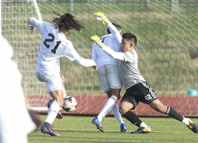 NWA Democrat-Gazette/BEN GOFF @NWABENGOFF Elliott Nimrod (21) of Bentonville High scores a goal as Rogers High goalkeeper Anthony Garcia (right) tries to get around Bentonville's Lucas Apparecido on Tuesday at the Tiger Athletic Complex in Bentonville.