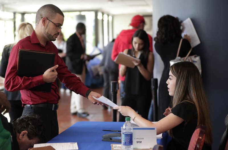 In this Jan. 30, 2018, file photo, an employee of Aldi, right, takes an application from a job applicant at a JobNewsUSA job fair in Miami Lakes, Fla. On Friday, April 6, the U.S. government issues the March jobs report. 