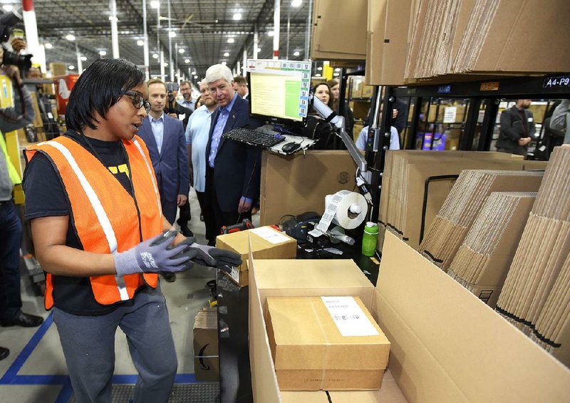 Anjoli Wilson packages products as Michigan Lt. Gov. Brian Calley (center) and Gov. Rick Snyder watch during the grand opening of Amazon’s new fulfillment center in Livonia in March.  