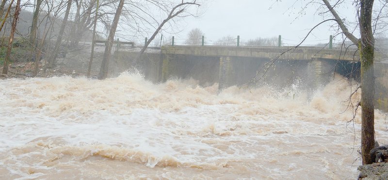 Keith Bryant/The Weekly Vista Floodwaters rush past the Lake Bella Vista Dam, just upstream from the streambank restoration project. The heavy rain that northwest Arkansas received late March, as well as other flood events, contribute to erosion of the creek bank.