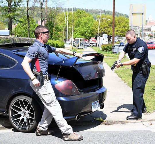 The Sentinel-Record/Grace Brown SUSPECT VEHICLE: Hot Springs police Detective Jarrett Cantrell, left, and Officer Tyler Cox check the trunk of a wrecked vehicle at the intersection of Malvern Avenue and Moore Street after the driver reportedly struck a fence and fled on foot while trying to evade an officer on Thursday.