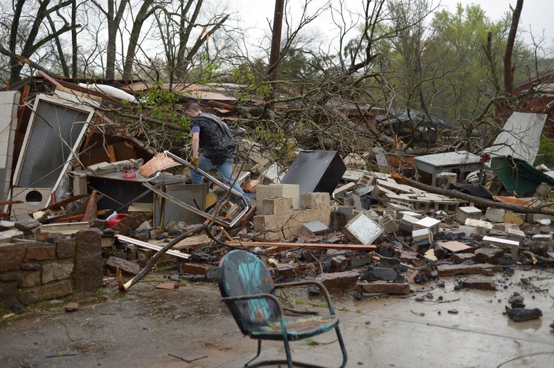 Matt Kimes of West Fork sorts through the rubble of a detached garage and home owned by his grandmother, Farnese Kimes, Friday, April 13, 2018, in downtown Mountainburg after a tornado swept through the town.