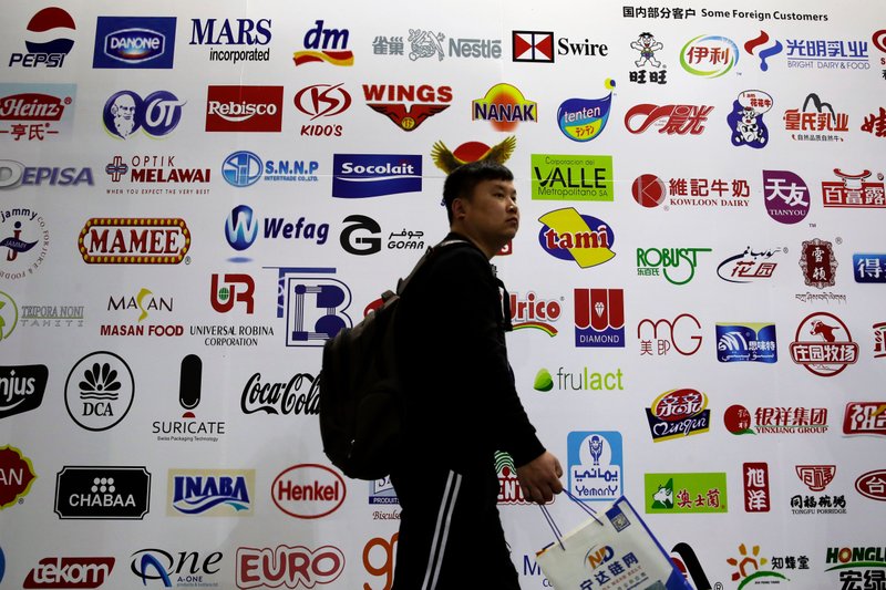 In this April 12, 2018, photo, a man walks by a billboard displaying a Chinese company developed packaging machinery for local and foreign food and beverage companies at the International soybean exhibition in Shanghai. Chinese soybean farmers, importers and processers say they are unconcerned about potential Chinese tariffs on American soybeans in an escalating dispute with the administration of President Donald Trump over trade and technology. (AP Photo/Andy Wong)