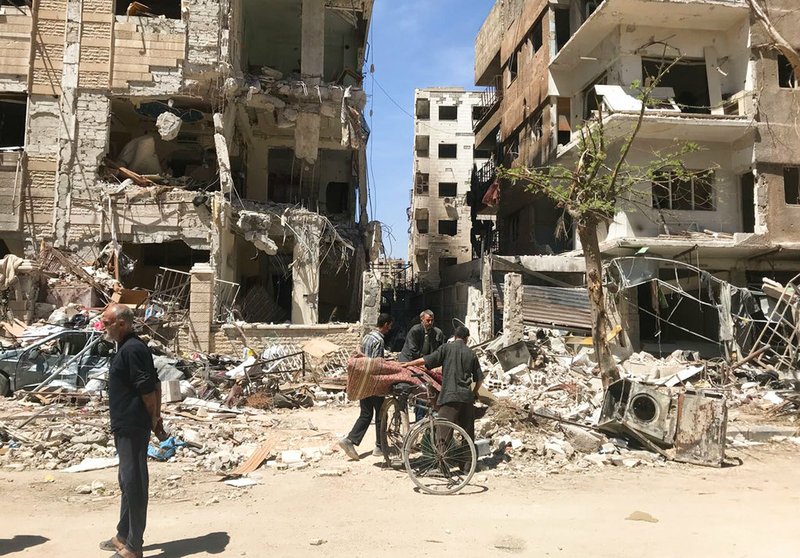 People stand in front of damaged buildings in the town of Douma, the site of a suspected chemical weapons attack, near Damascus, Syria, on Monday, April 16, 2018.