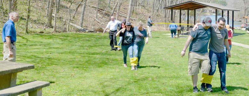 Keith Bryant/The Weekly Vista Bella Vista police chief James Graves (left) stands at the turnaround point as dispatchers tackle the three-legged race. Fire Chief Steve Sims, background, works with Leslianne Pratt just behind dispatcher Jamie Abbott and dispatch supervisor Christy Terry, both teams trying to catch up with dispatchers Blake Hendricks and Nick Collins, who are attempting to turn around.
