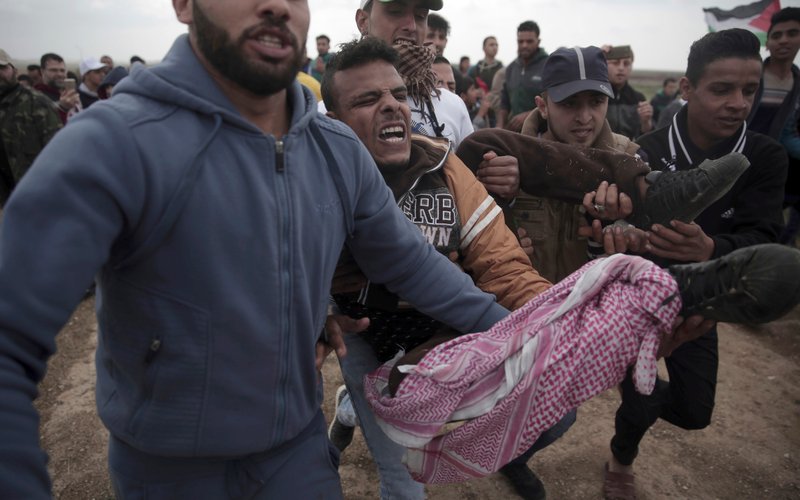 FILE - In this Friday, March 30, 2018 file photo, Palestinian protesters carry a wounded man that was shot by Israeli troops during a demonstration at the Gaza's border with Israel. The flareup of deadly violence in Gaza is of a new kind, even in the inventive annals of Mideast conflicts: Israeli soldiers shooting at Palestinian demonstrators burning tires and hurling firebombs across what looks like an international border, inflicting casualties while claiming concerns of a mass breach of the barrier. (AP Photo/Khalil Hamra, File)