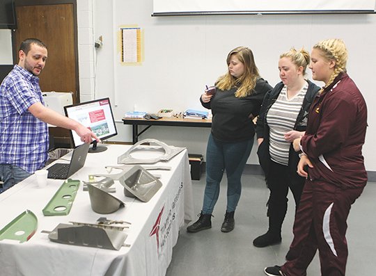 The Sentinel-Record/Richard Rasmussen INDUSTRY LEADERS: Justin Vik, left, training manager at Triumph Precision Components, talks about some of the airplane parts his company makes with Lake Hamilton High School students Taylor Morris, Alex Nash and Samantha Springer, right, during National Park College's Aerospace Day Tuesday. Groups of students from area high schools learned from local aerospace companies about what they do and explained the different career opportunities they offer.