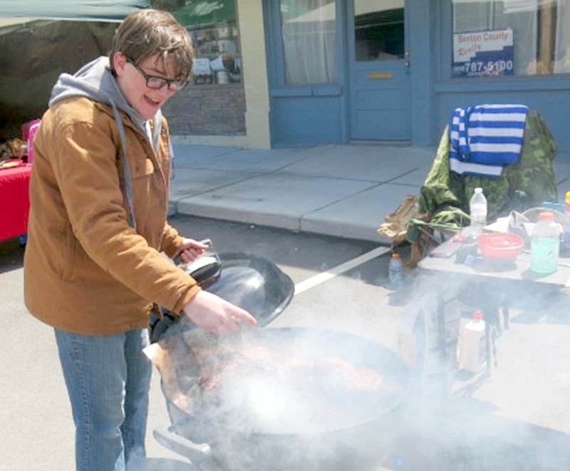 James Douglass, 15, of Bentonville, is surrounded by a cloud of smoke as he turns pieces of pork shoulder he is preparing at the second annual Smoke on the Border BBQ competition, Saturday, April 7. James placed seventh in the Kid’s Q burger competition, 10 and over division, on Saturday afternoon.