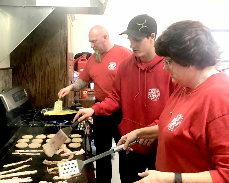 Photo by Sally Carroll Pineville marshal Chris Owens (back, right) and volunteer firefighters Jake Leake and Lori Byrd cook up some tasty breakfast at the Pineville Rural Fire Department's fundraiser on April 7.