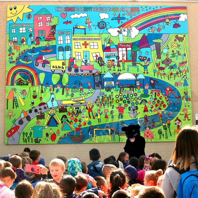 Janelle Jessen/Siloam Sunday Kindergarten students from Northside Elementary School sang along with Shadow the panther mascot during the reveal of the mural they created. The new mural is the result of a collaboration between the school, Main Street Siloam Springs, Art Feeds and Arvest Bank. It is located on the side of the Arvest Bank building at the corner of University Street and Broadway Street.