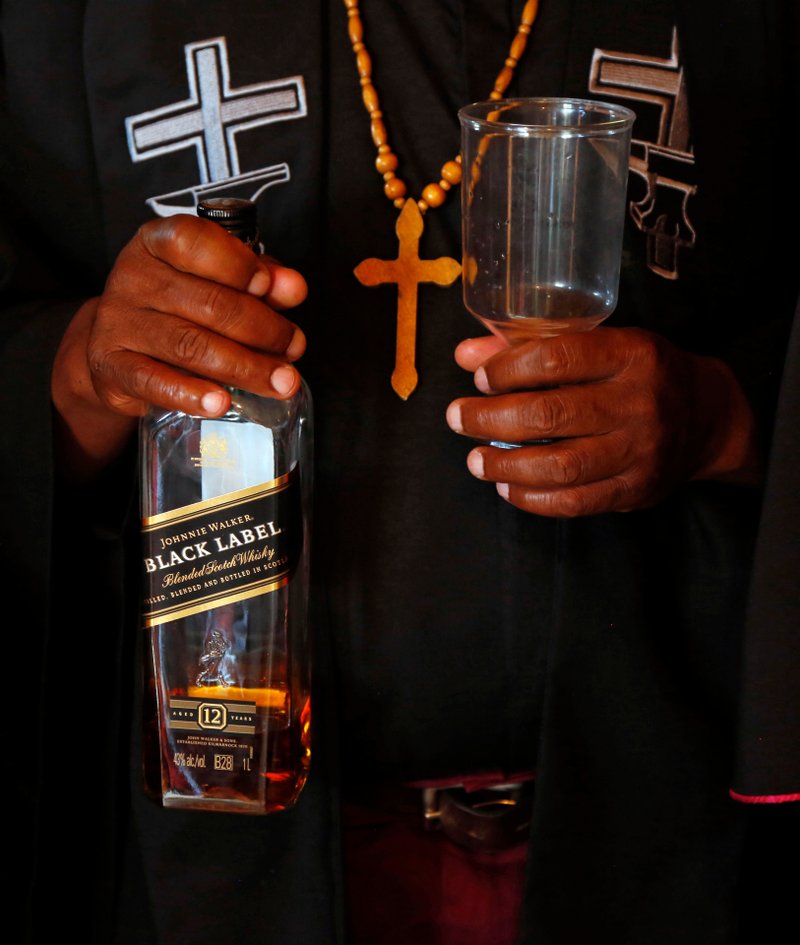 A bottle of whiskey is prepared to anoint a priest with whiskey into the Gabola Church during a service in a bar in Orange Farm, south of Johannesburg Sunday, April 15, 2018. The new church in South Africa celebrates drinking alcohol and holds enthusiastic, alcohol fuelled services in bars, for those who have been rejected by other churches because they drink alcohol. (AP Photo/Denis Farrell)