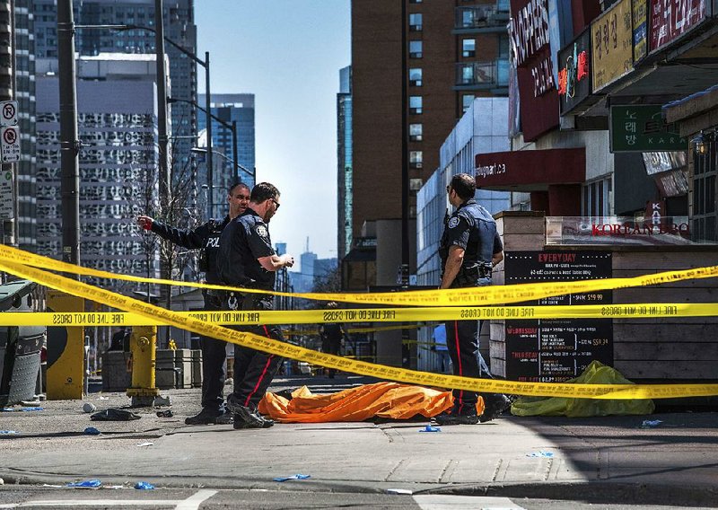 Police officers stand by a covered body Monday in Toronto after a van drove onto a sidewalk and crashed into a crowd of pedestrians. 
