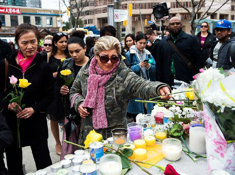 Ozra Kenari joins others Tuesday in placing flowers at a memorial for the victims of Monday’s van attack in Toronto.  