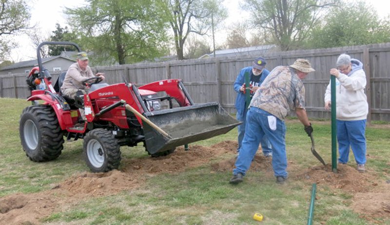 Westside Eagle Observer/SUSAN HOLLAND Members of the Gravette Lions Club held a work day Saturday, April 21, to begin construction on the city's new human foosball court at Pop Allum Park. Jerry Hallum, of Colcord, Okla., delivers a batch of concrete in the scoop of his tractor as Lion Jeff Davis checks to see that the last post is level and Lion Al Blair shovels concrete around a post while Lion Sue Rice holds it steady.