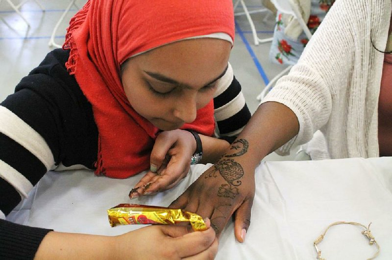 Mariam Khan (left) applies a temporary henna tattoo to the hand of Janecia Collins at the 2017 Little Rock International Food Festival. 