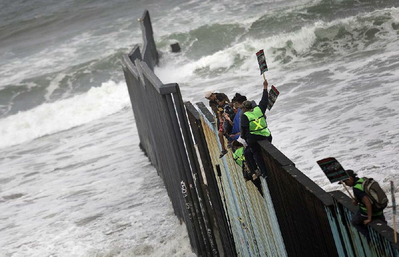 Central American migrants traveling with a caravan sit Sunday atop the border wall separating Tijuana, Mexico, and San Diego at the spot where the wall ends in the Pacific Ocean. The asylum seekers’ arrival Sunday drew supporters from both sides of the border. 

