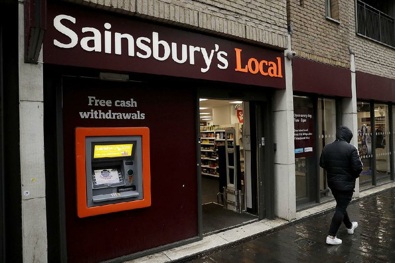 A pedestrian passes a Sainsbury’s Local grocery store on Monday in London. With its plan to buy Walmart’s Asda chain, Sainsbury’s aims to create a merged company with $70 billion in U.K. sales. 
