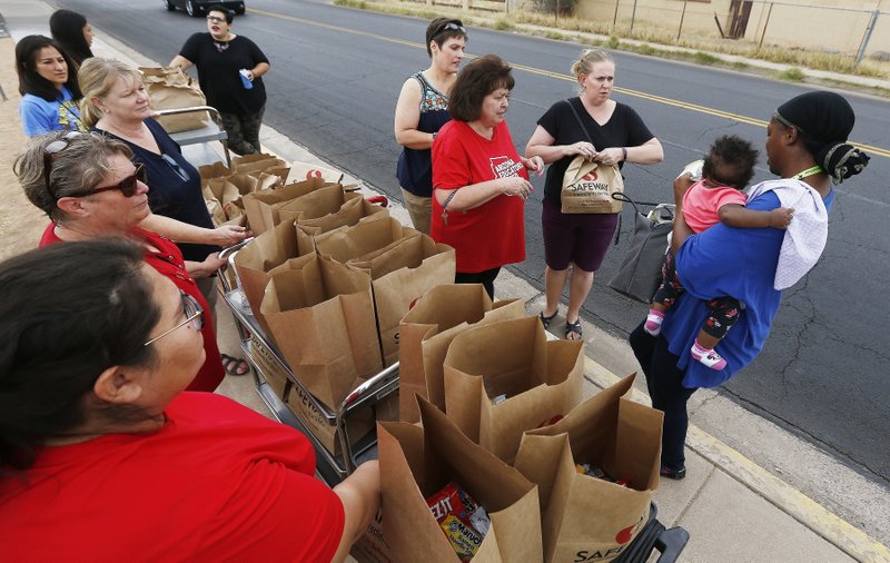 Teachers at Webster Elementary School stand out in front of the school as they hand out free food bags they donated for their students and families as the statewide teachers strike enters a fourth day, Tuesday, May 1, 2018, in Mesa, Ariz. (AP Photo/Ross D. Franklin)