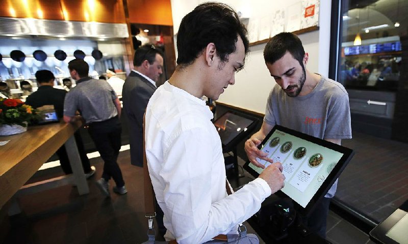 Charles Renwick, lead software engineer at Spyce Food Co. (right), assists a customer Thursday with an order at Spyce, a new restaurant in Boston that uses robotics to prepare meals. 
