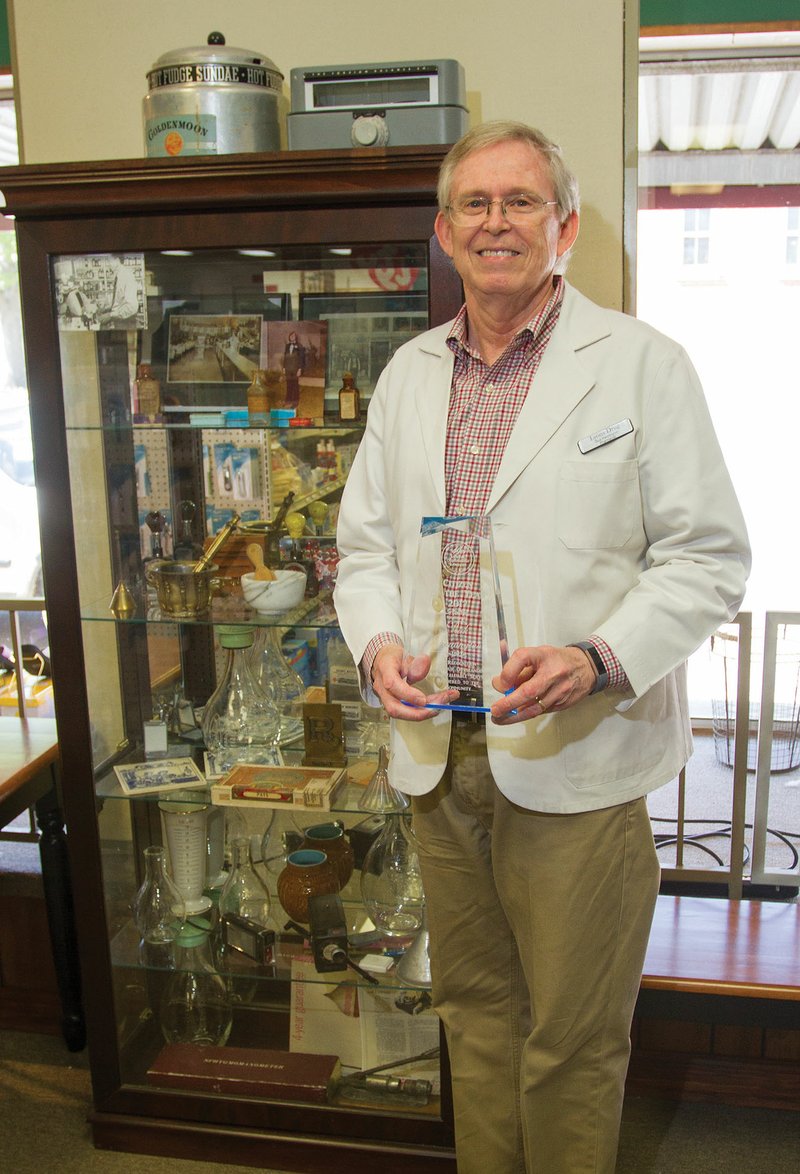 Rick Pennington of Lonoke stands next to a display of pharmacy collectibles while holding his award for being named the Lonoke Area Chamber of Commerce Citizen of the Year. Pennington has been a pharmacist at Lyons Drug Store for close to 44 years, and purchased the store 13 years ago.
