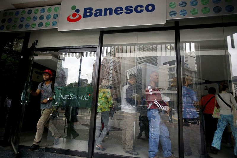 A customer leaves a Banesco bank branch Friday as others wait in line in Caracas, Venezuela.  